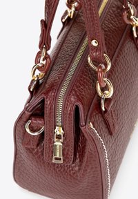 Bordowa skórzana torebka o teksturowanym wykończeniu, z elementami w kolorze złotym, podwójnymi uchwytami i wyraźnym zamkiem błyskawicznym u góry.