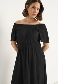 Schulterfreies schwarzes Kleid mit einem gerafften Oberteil, kurzen Ärmeln, fließendem Rock und strukturiertem Stoff.