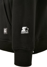 Černá mikina se žebrovanými manžetami a lemem. Na rukávu je bílý vyšívaný logo "STARTER" se hvězdou. Měkký materiál z bavlny.