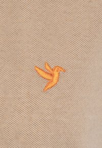 Beige gebreide stof met een geborduurd oranje vogelontwerp, waarbij een gestructureerd oppervlak met gedetailleerde stiksel wordt getoond.