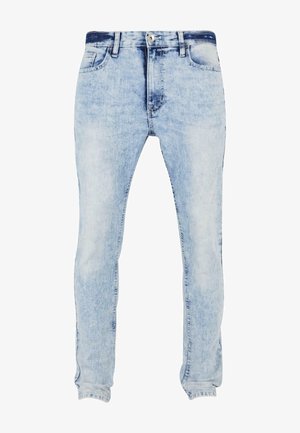 Jeans de mezclilla de color azul claro con lavado desgastado, diseño ajustado, estilo de cinco bolsillos y cierre de botón con cremallera. Textura desgastada en la tela.