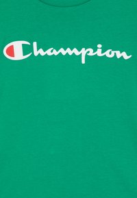 Zelené bavlnené tričko s veľkým bielym logom "Champion" a kruhovým červeným akcentom pri "C". Hladká textúra, dizajn s okrúhlym výstrihom.