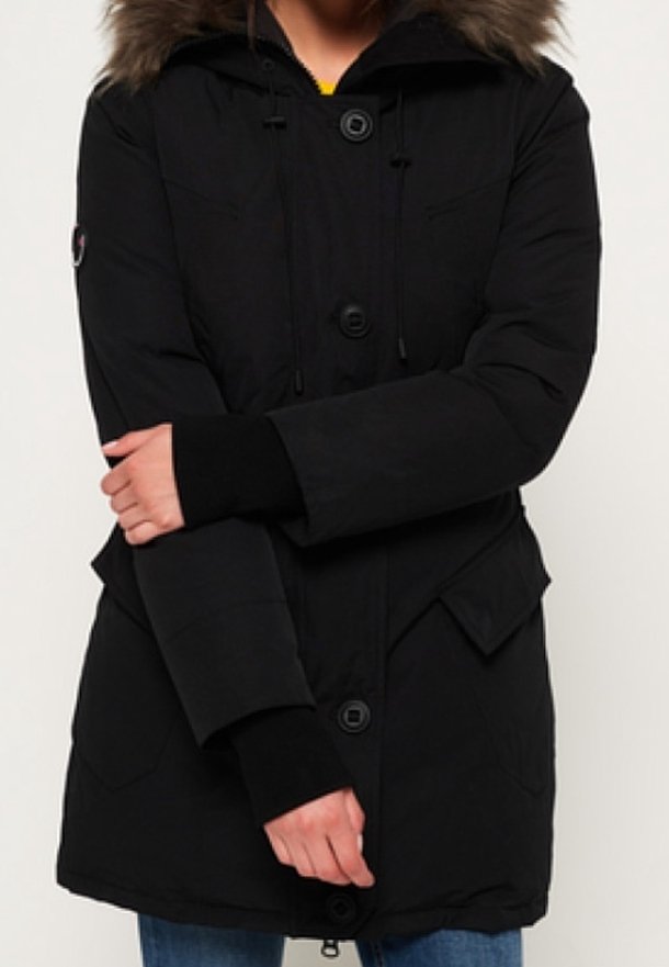 Zwarte parka jas met een capuchon van fauxbont, rits- en knoopsluiting, elastische manchetten en voorzakken. Gemaakt van een duurzame, gestructureerde stof.
