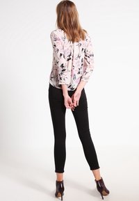 Blusa con motivo floreale in rosa chiaro con foglie nere, abbinata a jeans skinny neri e stivali con tacco a piacere bordò.