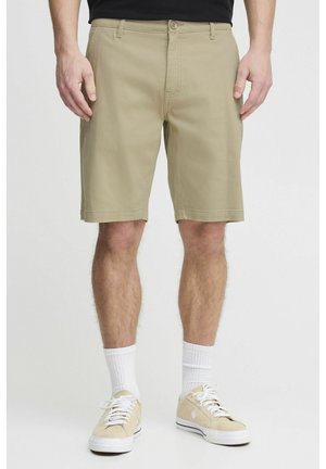 Shorts beige avec une coupe droite, des poches avant et une fermeture à bouton. Associés à des baskets claires et des chaussettes blanches à mi-mollet.