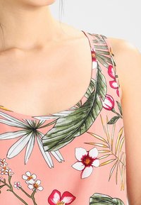 Débardeur fleuri avec un fond rose, des feuilles vertes et des fleurs multicolores. Tissu léger avec un col en rondeur.