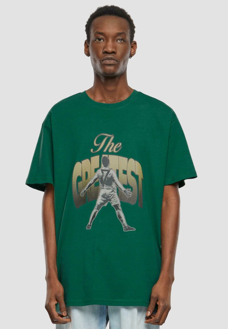Grøn bomulds t-shirt med en afslappet pasform, prydet med et centralt grafisk motiv af en fodboldspiller og teksten "The GREATEST" i fed gul.