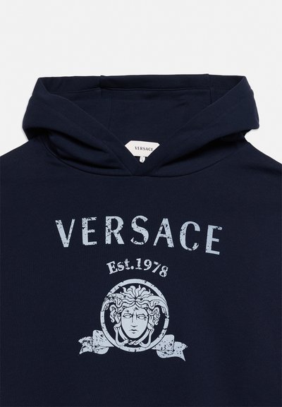Μπλε σκούφο με κουκούλα με το κείμενο "VERSACE", κάτω από αυτό "Est. 1978" και το λογότυπο κεφαλής Μέδουσας σε ανοιχτό μπλε στο μπροστινό μέρος.