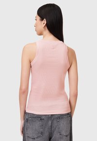 Top a canottiera rosa chiaro a coste con scollo rotondo e spalline larghe. Ha una silhouette aderente e una texture liscia, abbinato a jeans neri.