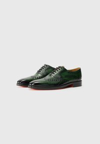 Green leather dress shoes with a smooth finish, featuring brogue detailing and a black toe cap, set on a flat sole with a red accent.