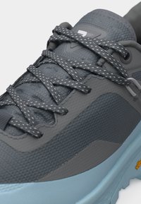 Zbliżenie na szaro-niebieskiego trampka z wzorzystymi sznurowadłami i teksturowaną cholewką, pokazującą część gumowej podeszwy z logo Vibram.