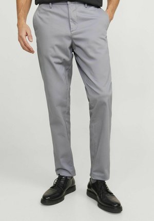 Pantaloni grigi slim-fit realizzati in tessuto liscio. Caratterizzati da tasche frontali e design a vita piatta. Indossati con scarpe in pelle nere.