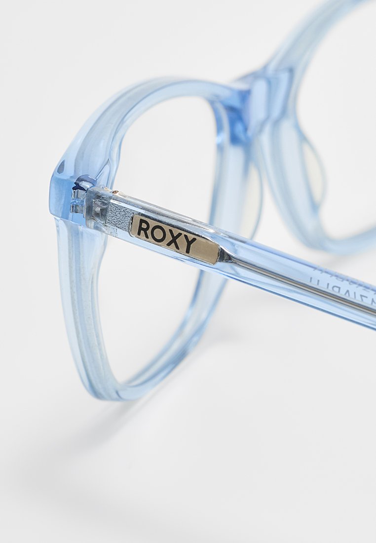 Gafas de sol de plástico transparente azul con forma cuadrada. Presentan un acento metálico en la patilla, etiquetado "ROXY".