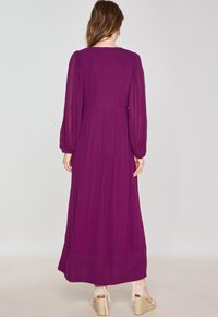 Abito viola a maniche lunghe con vita arricciata, tessuto fluido e orlo inferiore uniforme. Presenta polsini elasticizzati e scollatura rotonda.