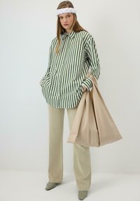 Cămașă cu dungi verzi și albe cu nasturi, asortată cu pantaloni evazați bej și o geantă mare bej; modelul poartă o bentiță albă împletită.