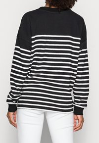 Schwarz-weiße gestreifte Langarmbluse mit lockerer Passform, ausgestattet mit einem gerippten Kragen und Manschetten. Glattes Material, lässiges Design.