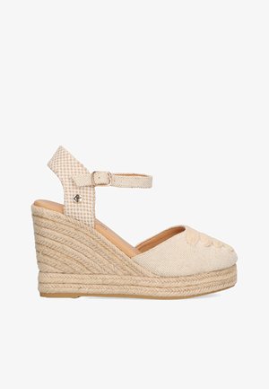 Sandalia cuña de esparto de color beige con parte superior de tela, plataforma de yute trenzado, tiras al tobillo y patrón decorativo de hojas en la zona de los dedos.