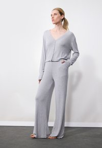 Set de loungewear gri deschis, texturat, format dintr-o bluză scurtă cu nasturi, mâneci lungi și pantaloni largi cu buzunare. Textură netedă.