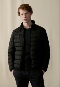Black puffer jacket with horizontal quilting, zip closure, and stand collar, worn over a black t-shirt. Texture appears smooth and lightweight.
