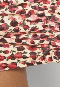 Tejido arrugado con un patrón floral en rojo, rosa y verde sobre un fondo crema. Material texturizado con rayas verticales y dobladillo terminado.