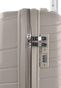 Maleta rígida de color beige claro con exterior texturizado, doble cremallera plateada y cerradura combinada incorporada. Cuenta con un diseño acanalado.