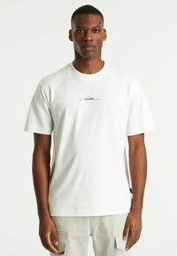 T-shirt bianco a maniche corte in un misto cotone, con una piccola stampa di testo nera sul petto. Design con collo a giro e vestibilità rilassata.