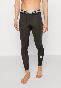 Leggings sportivi neri in materiale elastico, con una fascia in vita PUMA e un piccolo logo bianco sulla parte inferiore della gamba.