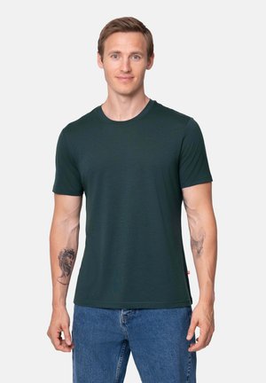 Dark green short-sleeve t-shirt made of soft fabric with a round neckline. Features a small red tag at the hem. Worn with blue jeans.