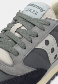 Sneaker grigia e blu navy realizzata in suede testurizzato e materiali in rete, con lacci verdi e un'etichetta logo sulla linguetta.