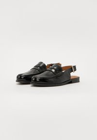 Svarte lær slingback-sko med rund tå, teksturert front og dekorativ sømdetaljering. Har en spenne-lukking og flat hæl.