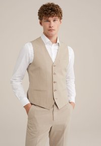 Beige Stoffweste mit fünf Knöpfen, einer einzelnen Brusttasche und zwei Fronttaschen. Getragen über einem weißen Hemd, das eine taillierte Passform und eine glatte Textur aufweist.