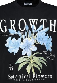 Black t-shirt with a floral graphic featuring blue flowers. Text includes "GROWTH IS ALL AROUND YOU" and "Botanical Flowers." Size label visible.