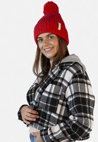 Red knitted beanie with pom-pom and tag, paired with a black-and-white plaid cropped jacket featuring a gray hoodie and one chest pocket.