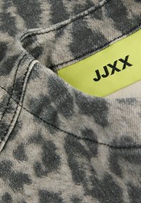 Grijze denimstof met een versleten patroon, met een afgeronde halslijn en een groene label met "JJXX" in het zwart gedrukt.