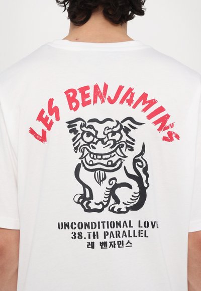 T-shirt blanc en coton avec un grand graphique noir représentant une créature semblable à un lion, accompagnée de texte rouge "LES BENJAMINS" et d'autres phrases en dessous.