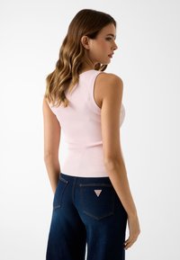 Débardeur côtelé rose clair associé à un jean large bleu foncé avec un patch logo triangulaire sur la poche arrière.