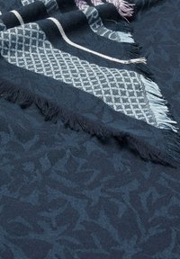 Navy blue woven scarf featuring a textured pattern, decorative fringes, and geometric accents in light blue and pink.