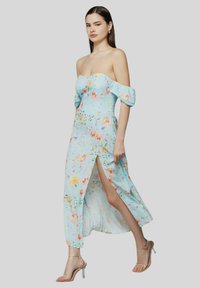 Vestito floreale azzurro senza spalline, con maniche scostate dalle spalle, spacco alto fino alla coscia e una silhouette fluida, caratterizzato da vivaci motivi floreali.