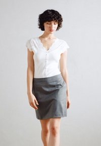 Hvit bluse med blonderkant ved skuldrene, knapping foran. Grå tettsittende skjørt, glatt tekstur. Enkel, klassisk design.