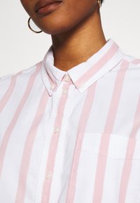 Striped button-up shirt featuring alternating white and pale pink horizontal stripes, a collar, and a single chest pocket. Soft cotton texture.
