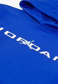 Felpa blu realizzata in morbido tessuto, caratterizzata da un grande logo bianco "JORDAN" e da una grafica in silhouette. Cappuccio e polsini a costine sono visibili.