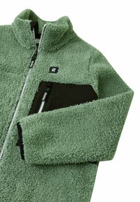 Giacca in pile verde spento, con colletto alto, tasca sul petto con zip nera e chiusure a zip a contrasto. Tessuto morbido e strutturato.