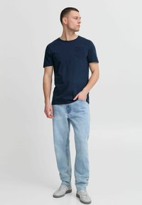 Tamsiai mėlynas medvilninis marškinėliai su trumpomis rankovėmis ir kišenėle, derinami su šviesiai mėlynomis džinsomis ir pilkų sportbačių. Paprastas, kasdienis dizainas.