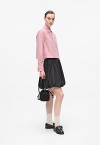 Chemise à rayures rouges et blanches, jupe plissée noire, mocassins noirs brillants, chaussettes crème et un petit sac noir avec des détails scintillants.