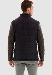 Herrjacka med en marinblå struktur kropp och mörkbruna puffy läderärmar, hög krage och en figursydd design.