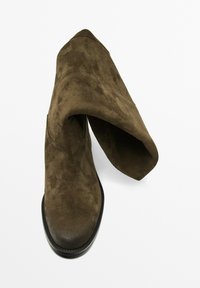 Bottines en daim vert olive foncé avec une texture douce, bout pointu et design de revers ; semelle noire avec détails de couture.