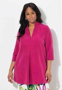 Fuchsia tuniek met een diepe V-hals, driekwart mouwen en geplooide voorkant. Zacht textuurstof, gecombineerd met gebloemde broek met patroon.