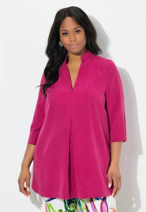 Fuchsia Tunika mit tiefem V-Ausschnitt, Dreiviertelärmel und plissiertem Vorderteil. Weicher Strukturstoff, kombiniert mit gemusterten Blumenhosen.