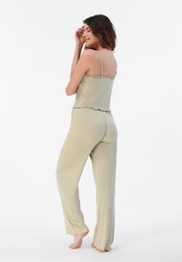 Conjunto de pijama verde claro con tirantes ajustables, bordes con volantes y pantalones holgados, que cuenta con una textura suave y lisa.