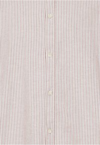 Gros plan sur le devant d'une chemise beige et blanche à rayures verticales avec des boutons blancs visibles au centre.